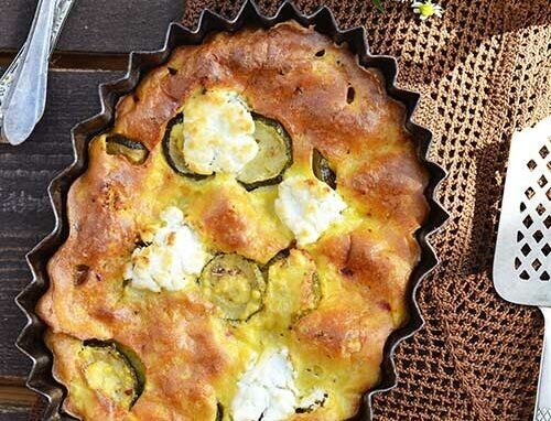 Une tarte à la courgette et au fromage dans un moule posée sur une table