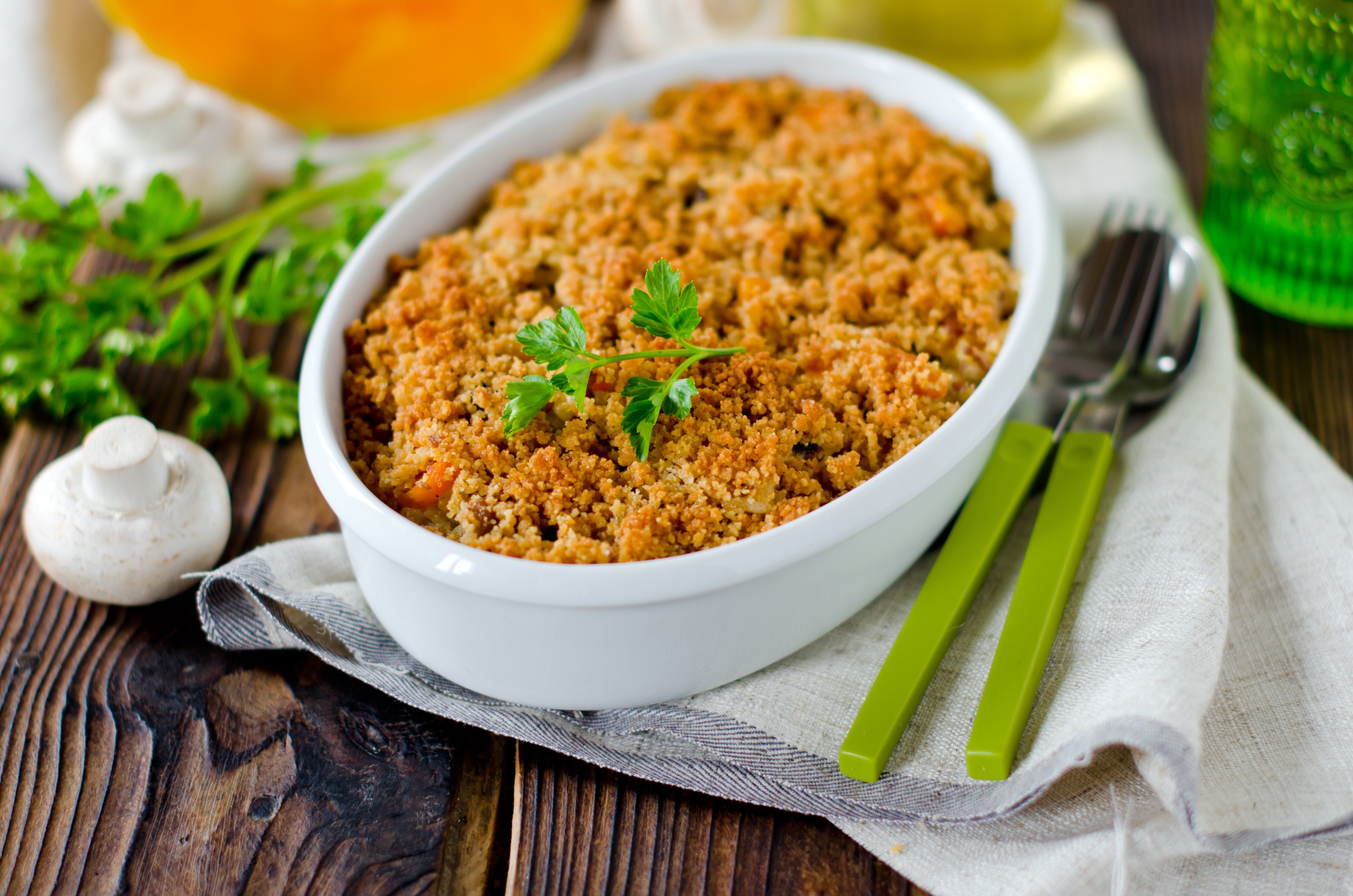 Un crumble de légumes présenté dans un plat blanc avec des couverts verts