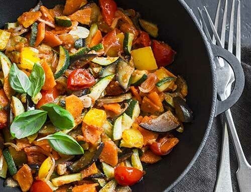 Une ratatouille servie dans un plat noir et deux fourchettes posés à côté